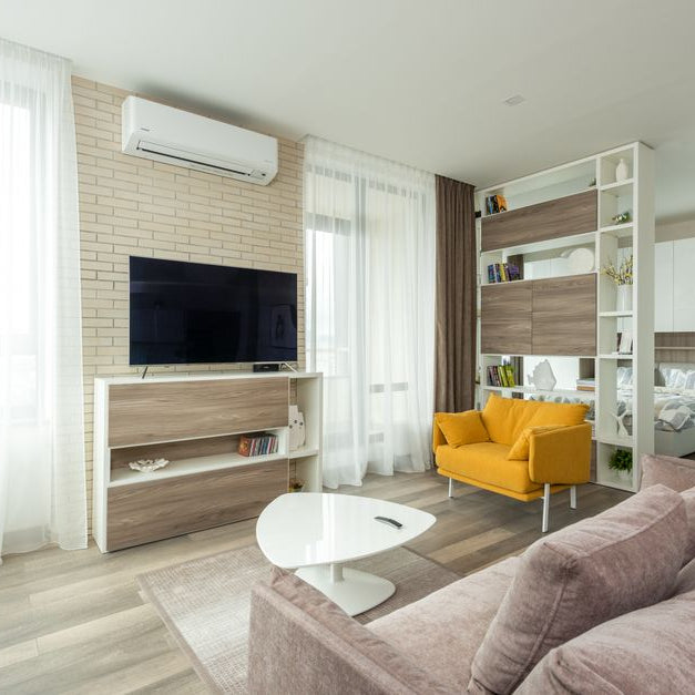 Cozy sofa and armchair placed near cabinet with TV set in contemporary living room separated from bedroom with cupboard and shelves in spacious studio apartment