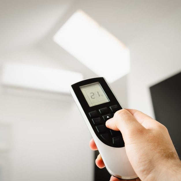 Close-up of a man using a remote to control air conditioning indoors.