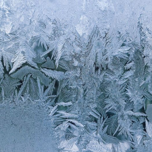 Close-up of intricate frost formations on glass, evoking a cold winter atmosphere.