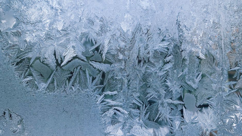 Close-up of intricate frost formations on glass, evoking a cold winter atmosphere.